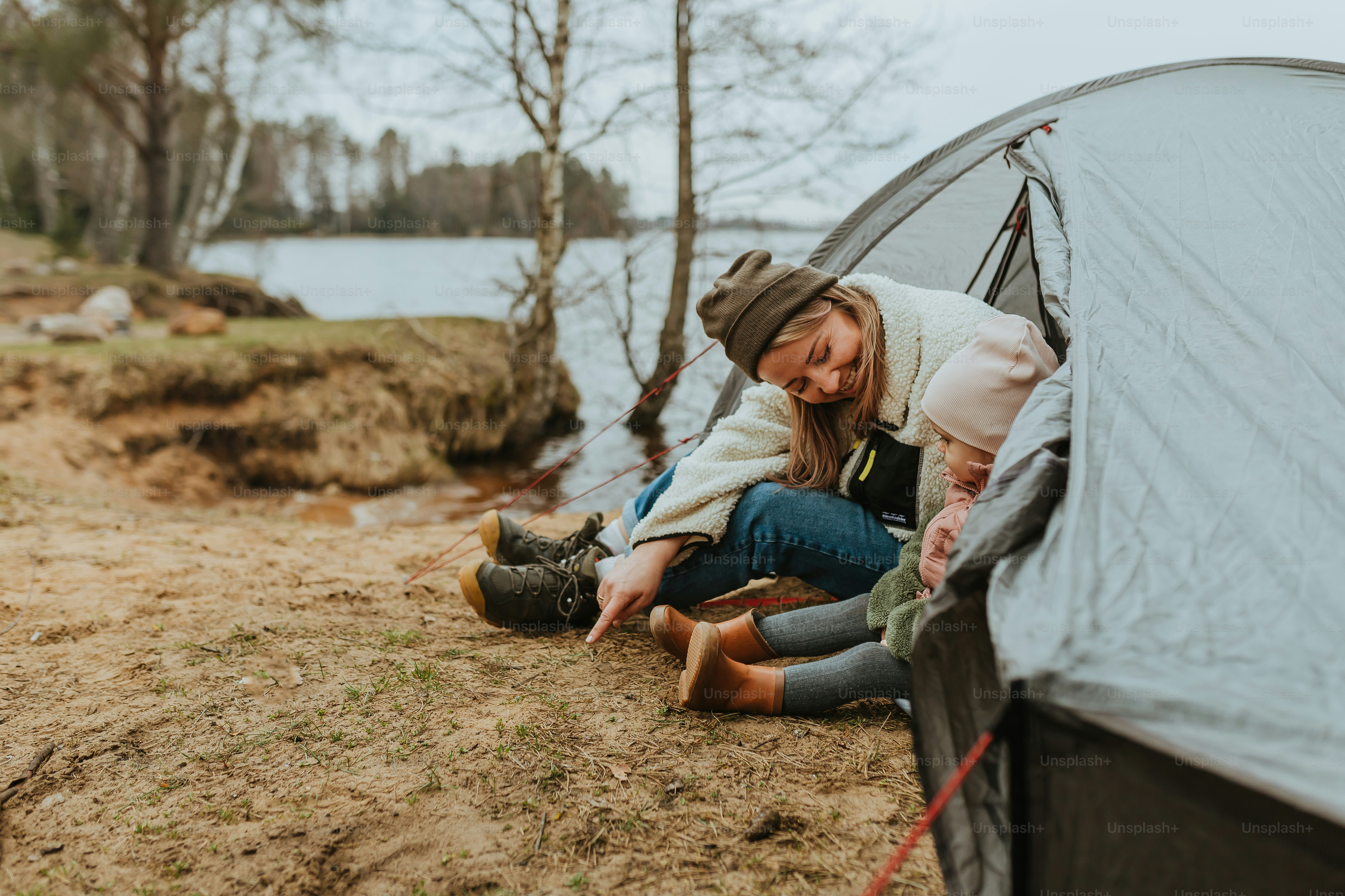 a woman sitting in front of a tent next to a lake