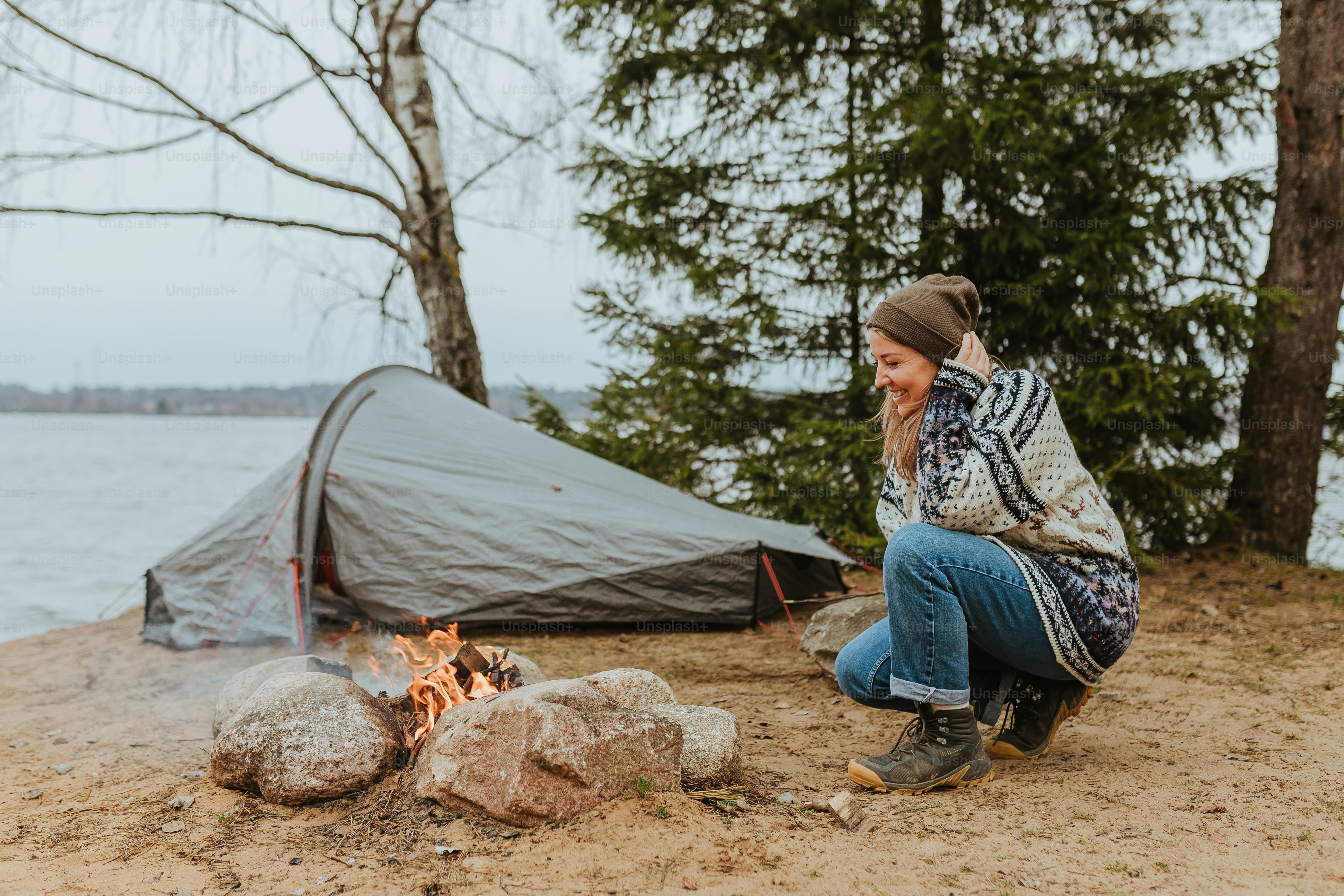 a woman sitting next to a campfire next to a tent