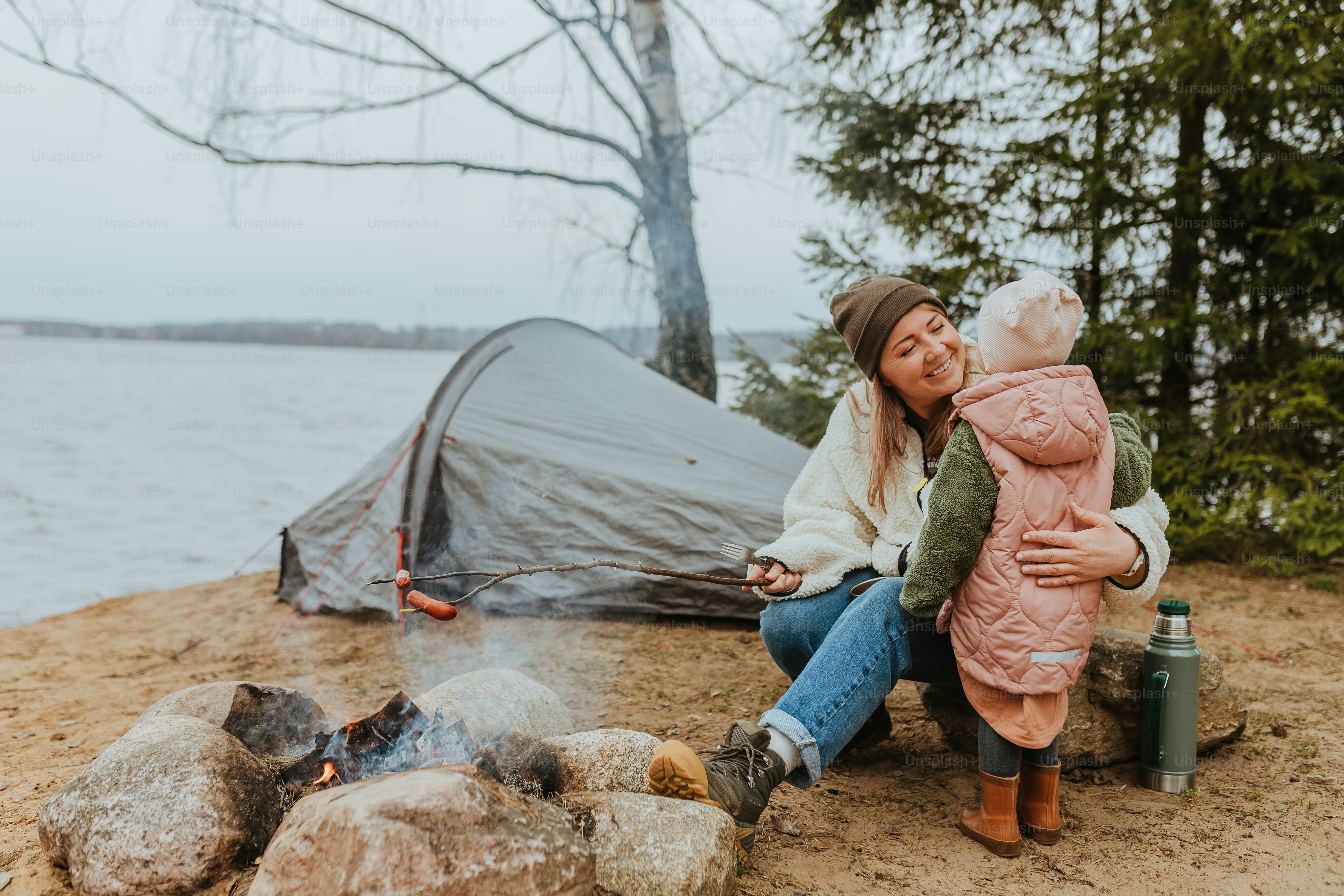 a woman holding a baby near a campfire