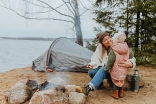 a woman holding a baby near a campfire