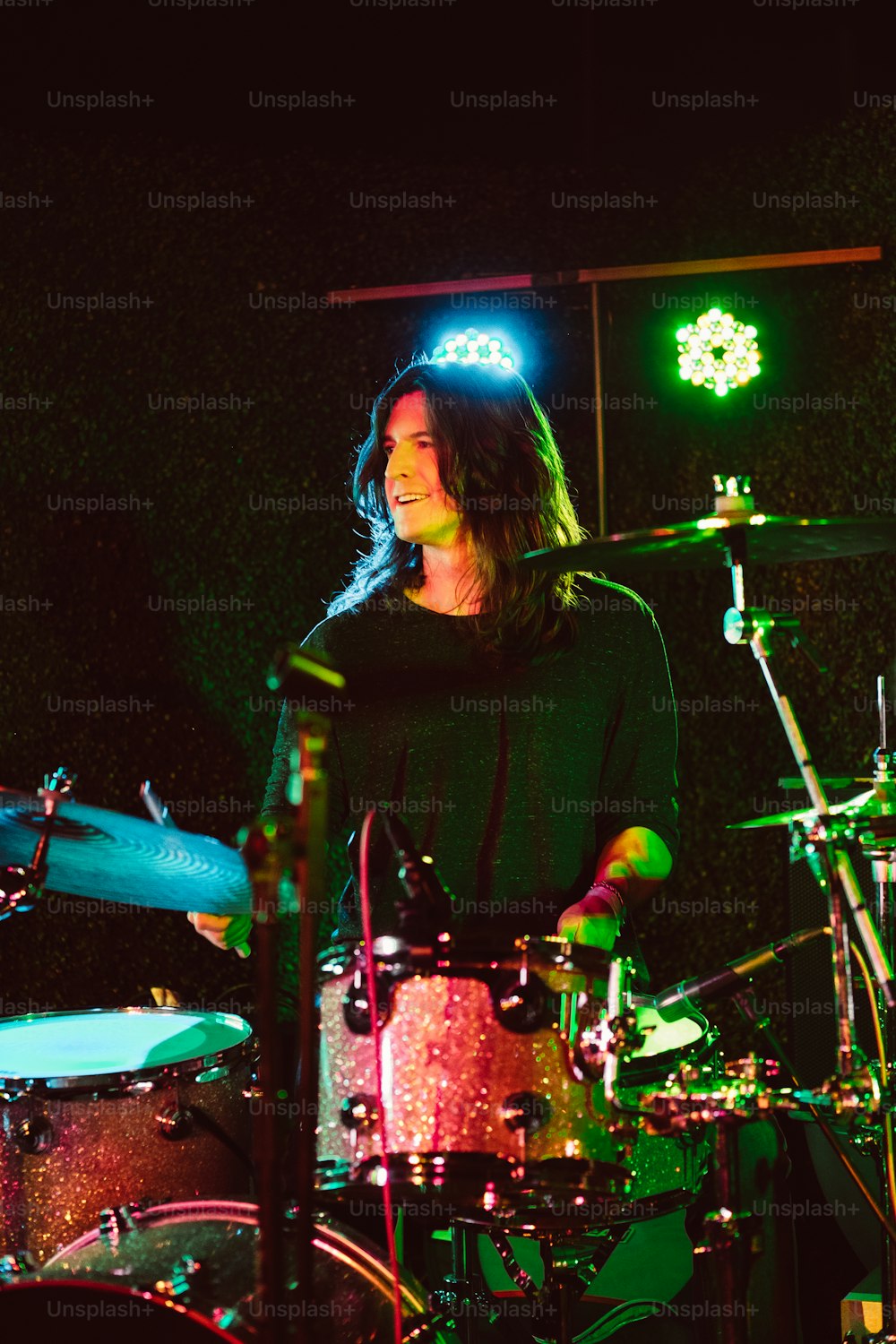 a man with long hair playing drums in a dark room