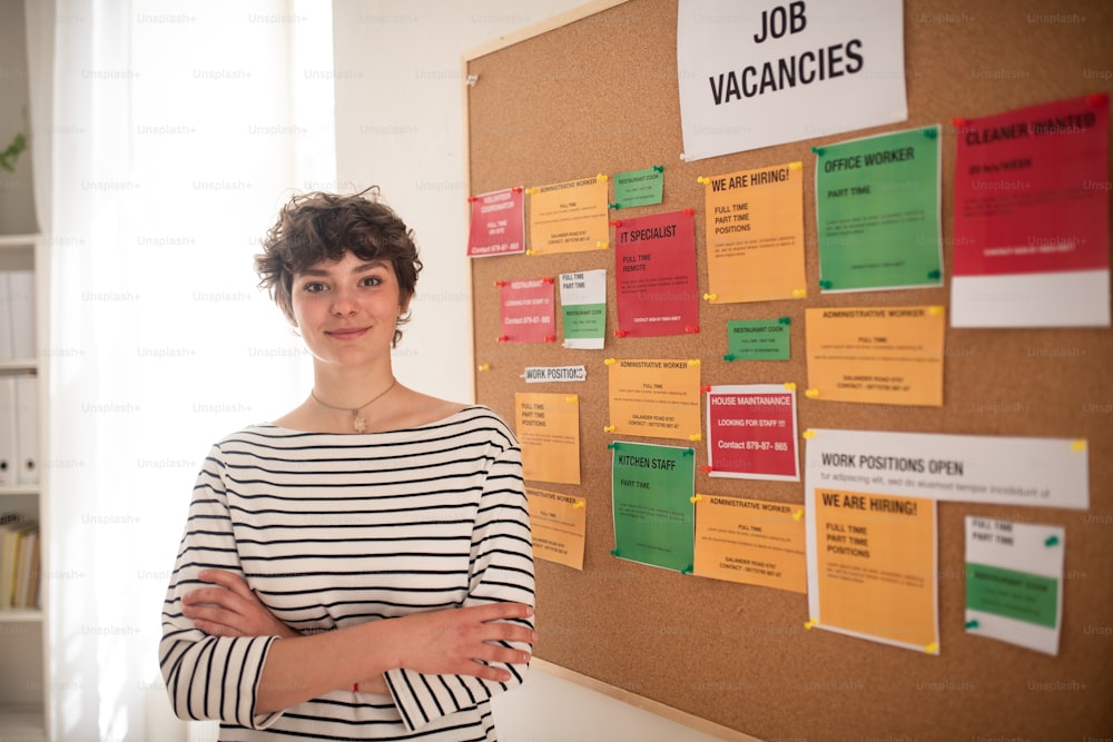 Una joven estudiante feliz parada frente al tablón de anuncios de empleo.