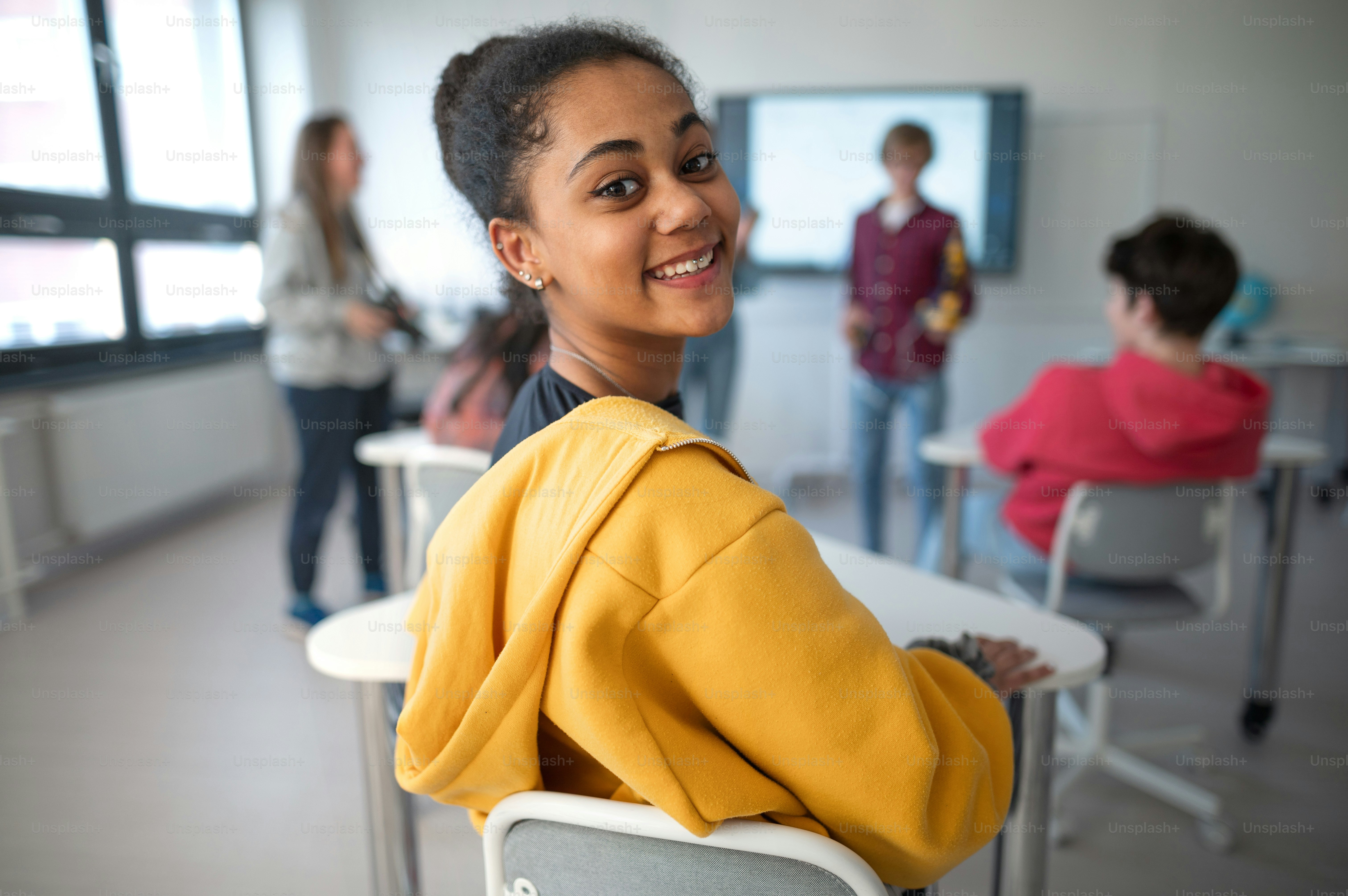 Happy college student sitting in school-desk and looking in camera.