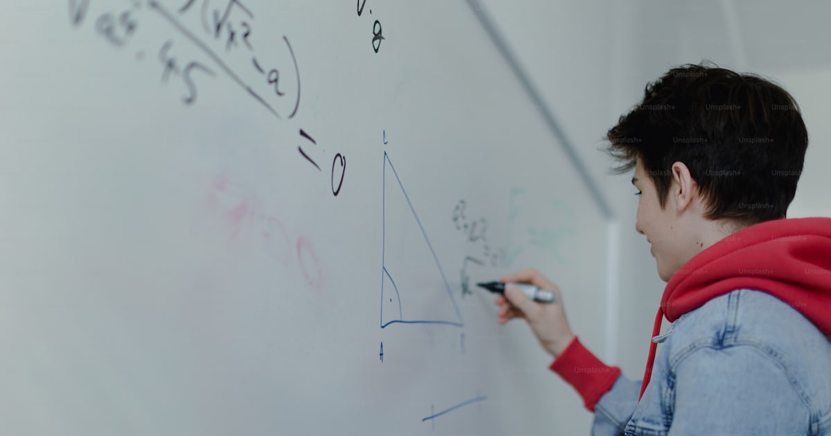 A back view of high school student solving math problem on whiteboard ...