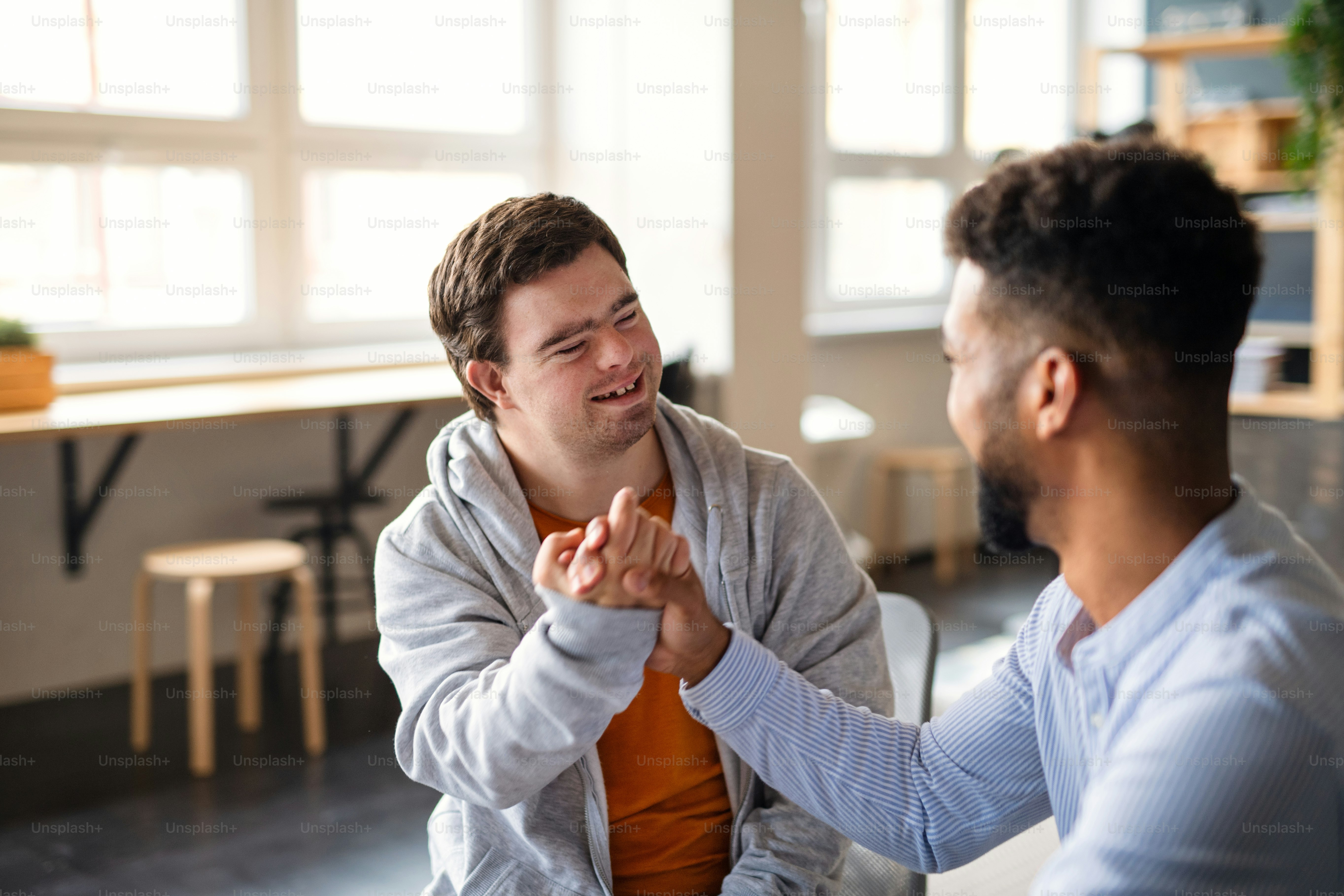 Un jeune homme heureux atteint du syndrome de Down avec son ami mentor célébrant le succès à l’intérieur à l’école.