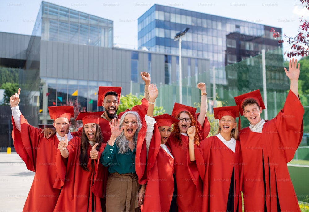 Un grupo de alegres estudiantes universitarios con el profesor celebrando al aire libre, mirando a la cámara, concepto de graduación.