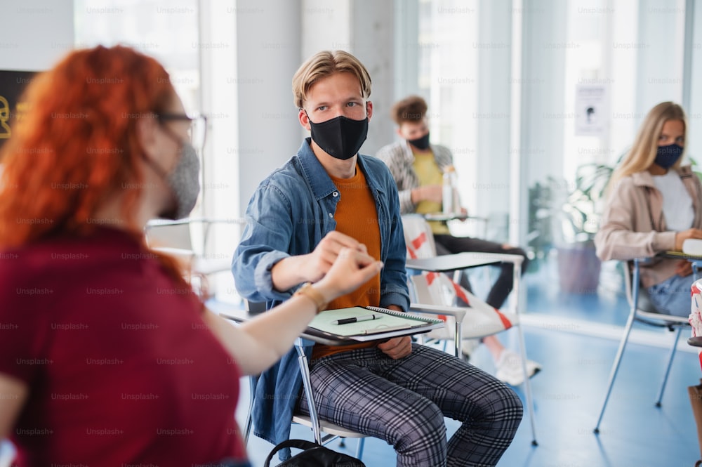 University students greeting in classroom indoors at school, coronavirus and back to normal concept.