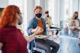 University students greeting in classroom indoors at school, coronavirus and back to normal concept.