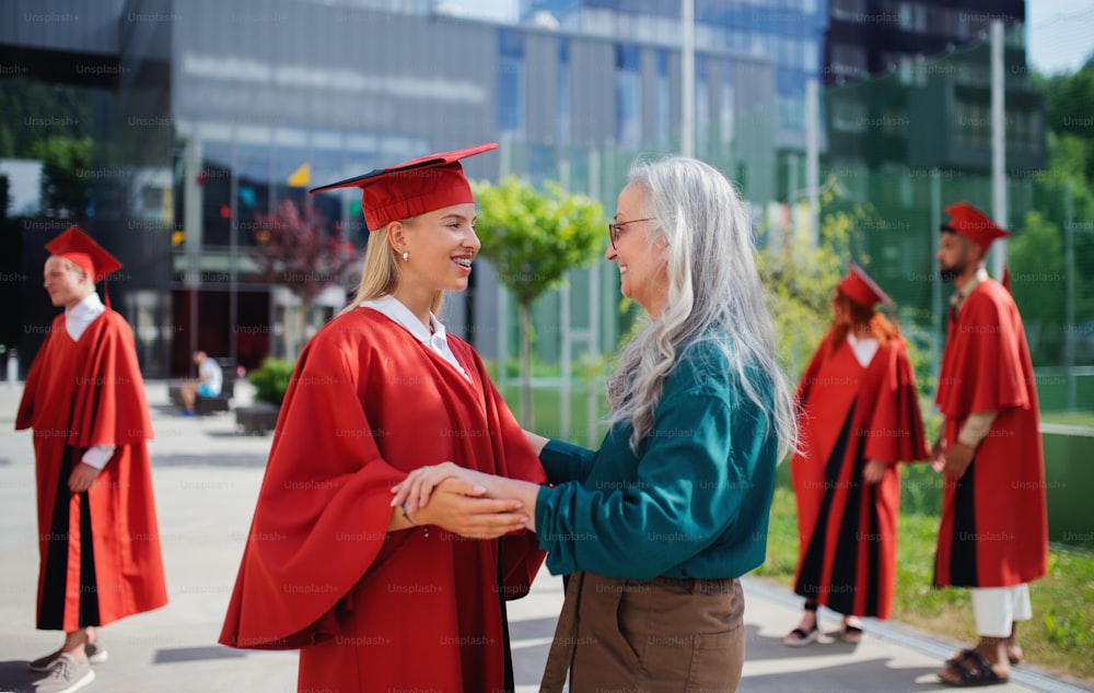 Un retrato de un alegre estudiante universitario con una madre celebrando al aire libre, concepto de graduación.