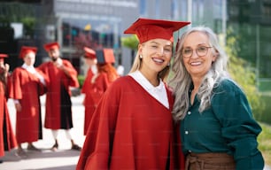 Ein Porträt einer fröhlichen Universitätsstudentin mit Mutter, die draußen in die Kamera schaut, Abschlusskonzept.