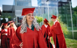 A portrait of cheerful senior woman student outdoors, graduation and third age university concept.