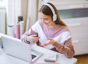 Junge Studentin mit Kopfhörern und Laptop am Tisch, Online-Unterrichtskonzept.