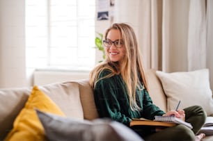 Uma jovem estudante feliz sentada no sofá, estudando. Espaço de cópia.