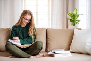 Uma jovem estudante feliz sentada no sofá, estudando. Espaço de cópia.