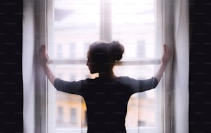 A rear view of young sad female student standing by window.