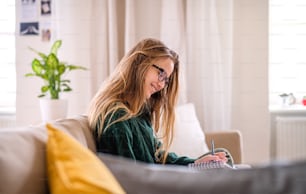 A happy young female student sitting on sofa, studying. Copy space.