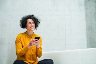 Portrait of a young student or businesswoman with smartphone sitting on desk in room in a library or office. Copy space.