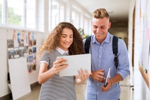 Joli couple d’adolescents dans le hall du lycée avec tablette, prenant un selfie.