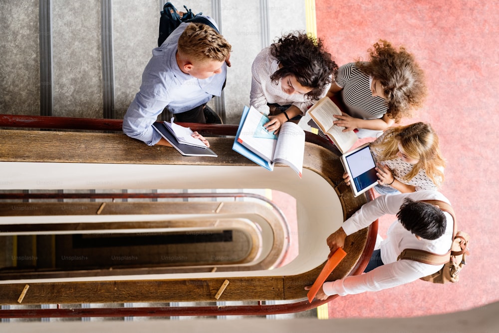 Group of attractive teenage students in high school standing on stairs, reading books.