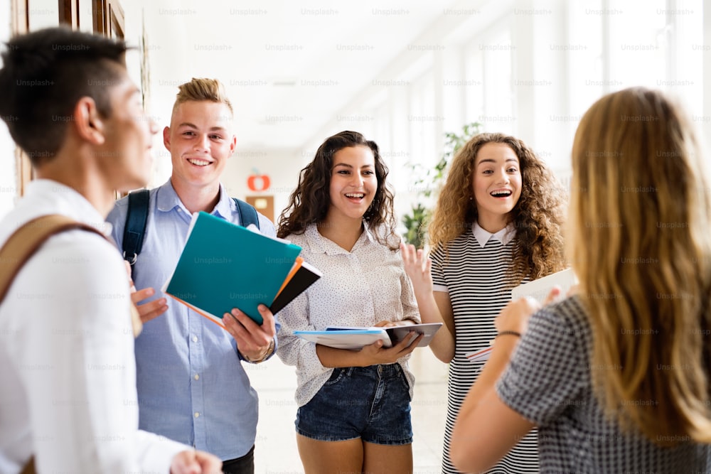 Grupo de estudiantes adolescentes atractivos caminando en el pasillo de la escuela secundaria, hablando juntos.