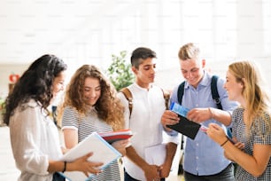Grupo de estudiantes adolescentes atractivos caminando en el pasillo de la escuela secundaria, hablando juntos.