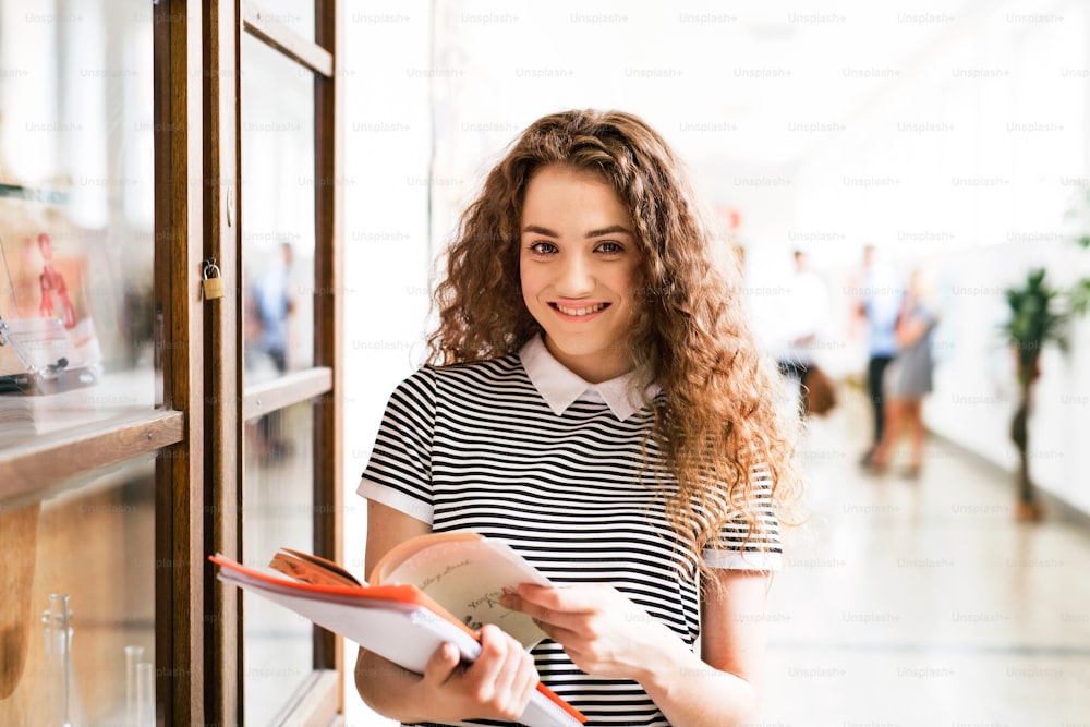 Attractive teenage girl with notebooks in high school hall during break.