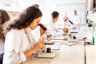 Belle lycéenne avec microscope en laboratoire. Enseignant principal enseignant la biologie.