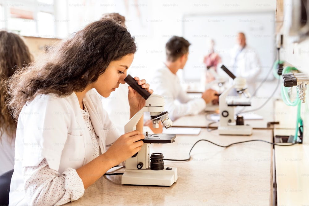 Beautiful high school student with microscope in laboratory. Senior teacher teaching biology.