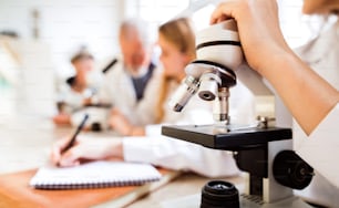 Nicht wiederzuerkennender Gymnasiast mit Mikroskop im Labor während des Biologieunterrichts.