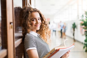 Attractive teenage girl with notebooks in high school hall during break.