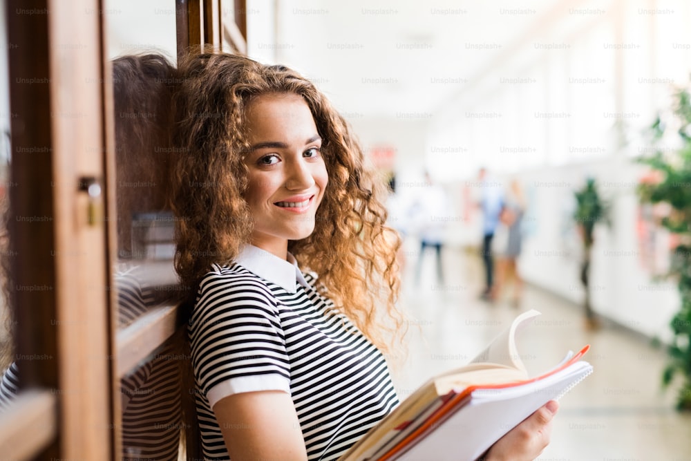 Attractive teenage girl with notebooks in high school hall during break.