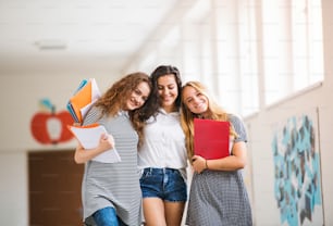 Grupo de tres atractivas adolescentes en el salón de la escuela secundaria durante el descanso, abrazándose y sonriendo.