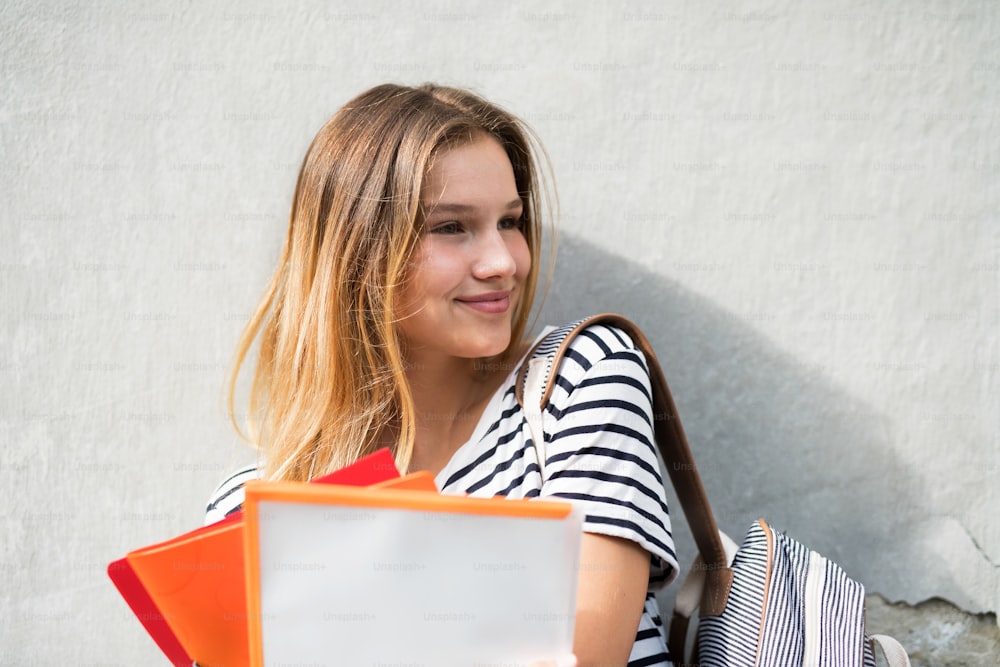Attraente studente adolescente in posa con quaderni e zaino davanti all'università.
