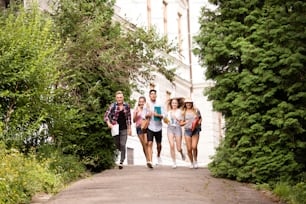 Group of four attractive teenage students running from university.