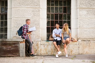 Group of attractive teenage students in front of university studying, talking together.