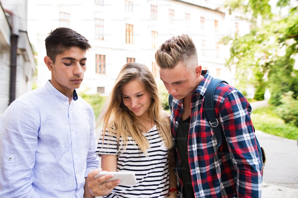 Grupo de estudantes adolescentes atraentes em frente à universidade tirando selfie com smartphone.