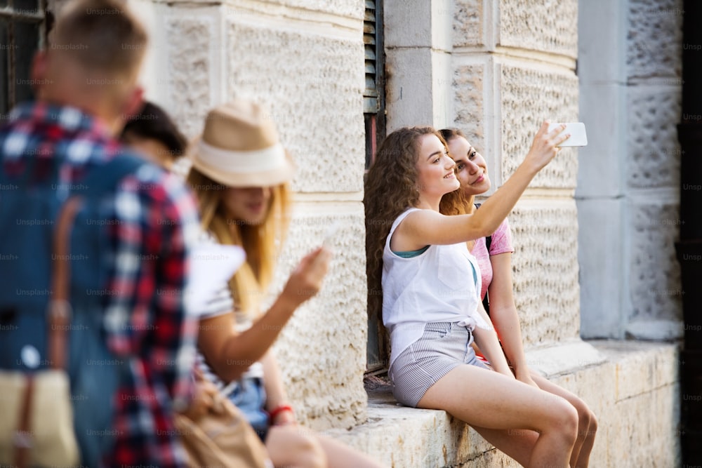 Estudiantes adolescentes frente a la universidad tomándose selfies con un teléfono inteligente.