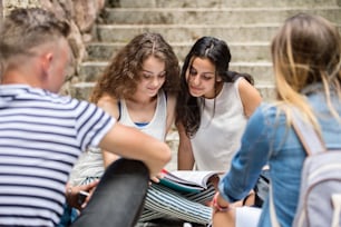 Grupo de cuatro atractivas estudiantes adolescentes sentadas en escalones de piedra frente a la universidad estudiando.