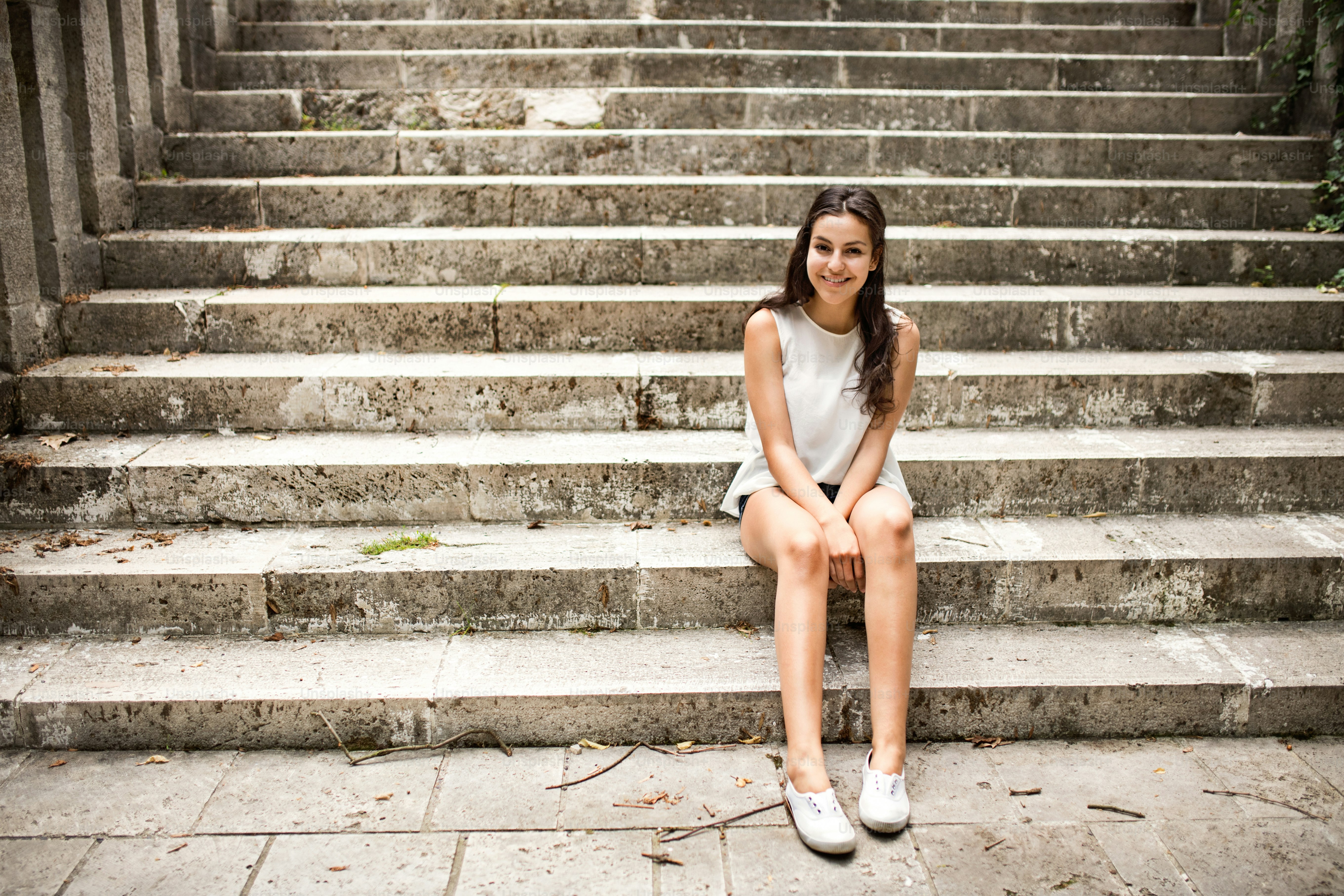 Menina estudante adolescente atraente sentada em degraus de pedra, sorrindo.