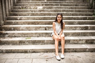 Attractive teenage student girl sitting on stone steps, smiling.