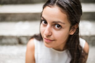 Gesicht eines attraktiven Teenager-Studentenmädchens, das lächelnd auf Steinstufen sitzt.