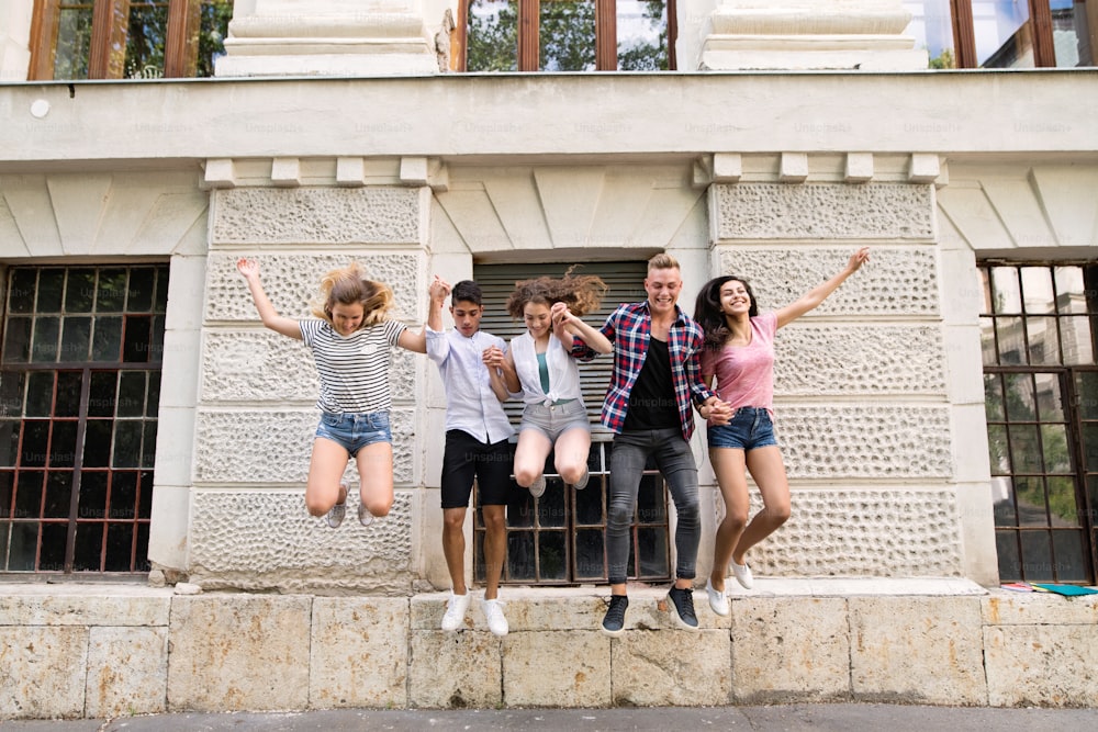 Agrupa a estudiantes adolescentes atractivos frente a la universidad saltando alto.