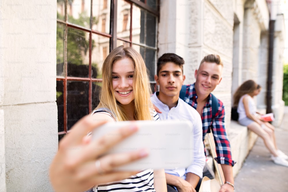 Agrupe estudantes adolescentes atraentes em frente à universidade tirando selfie com o smartphone.