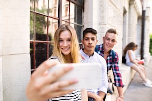 Gruppieren Sie attraktive Teenager vor der Universität, die Selfies mit dem Smartphone machen.
