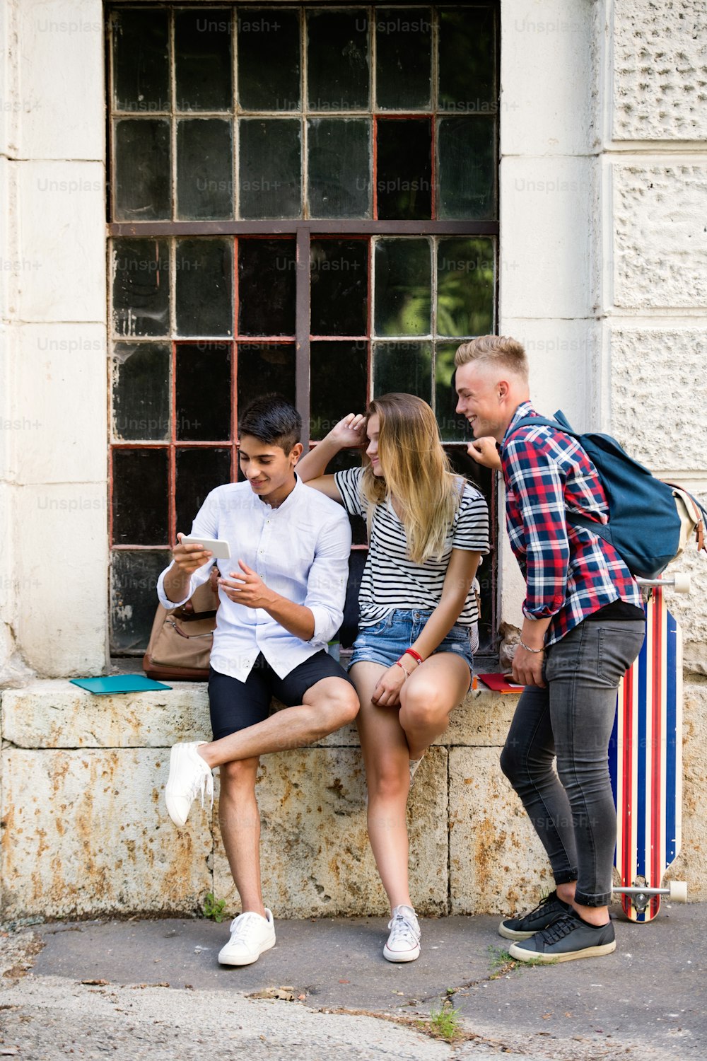 Gruppe attraktiver Teenager vor der Universität mit Smartphone, die etwas beobachten oder lesen.