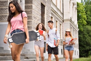 Group of four attractive teenage students walking to university.