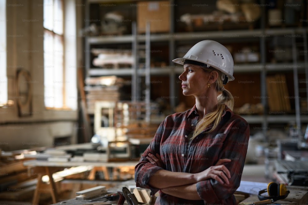 大工仕事場で屋内で腕を組んで脇を見ている女性エンジニアのポートレート。中小企業のコンセプト。