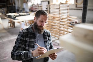A portrait of mature male carpenter sketching design of his product indoors in carpentery workshop. Small business concept.