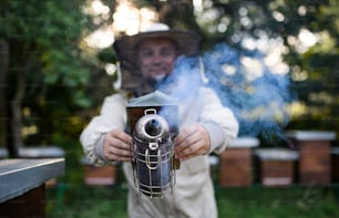 Portrait d’un apiculteur travaillant dans un rucher, utilisant un fumoir d’abeille.
