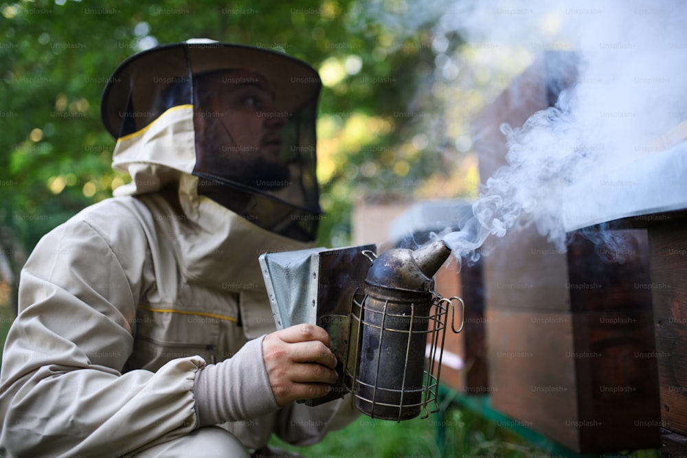 Ein Porträt eines Imkers, der in einem Bienenhaus arbeitet und einen Bienenraucher verwendet.